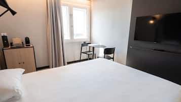 A hotel room with a bed, a desk with a chair, a television, and a window with curtains.