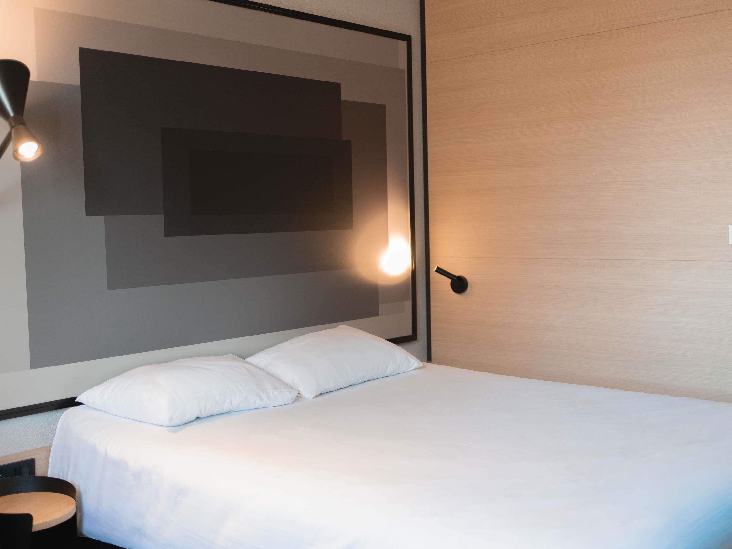 Een moderne hotelkamer met een groot bed, een nachtkastje en een wandlamp.