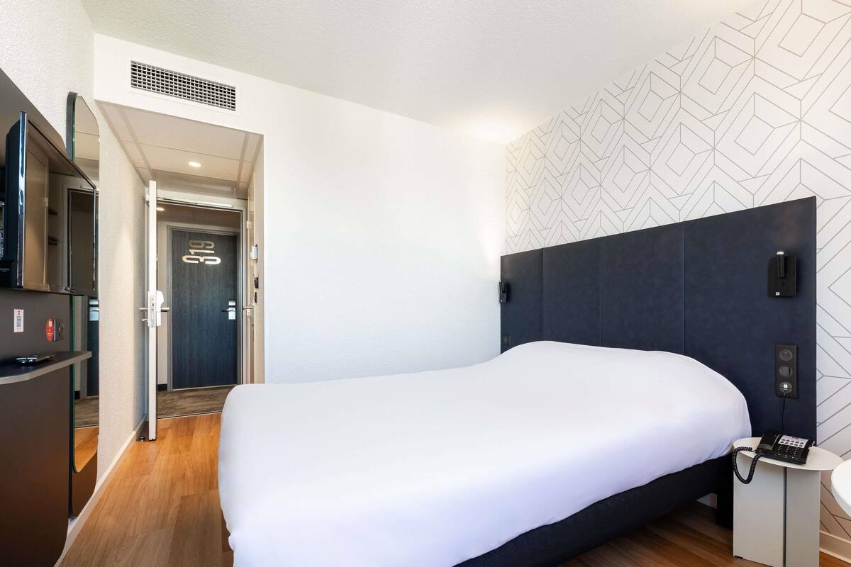 Une chambre d’hôtel moderne avec un grand lit, un téléphone sur la table de chevet et une petite table.