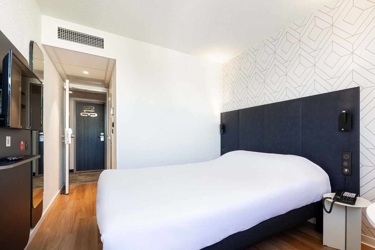 Une chambre d’hôtel moderne avec un grand lit, un téléphone sur la table de chevet et une petite table.