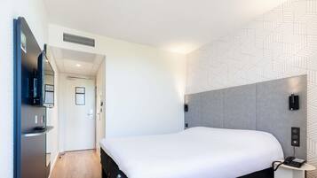 A modern hotel room with a large bed, a flat-screen TV, a small bedside table, and a patterned wall.
