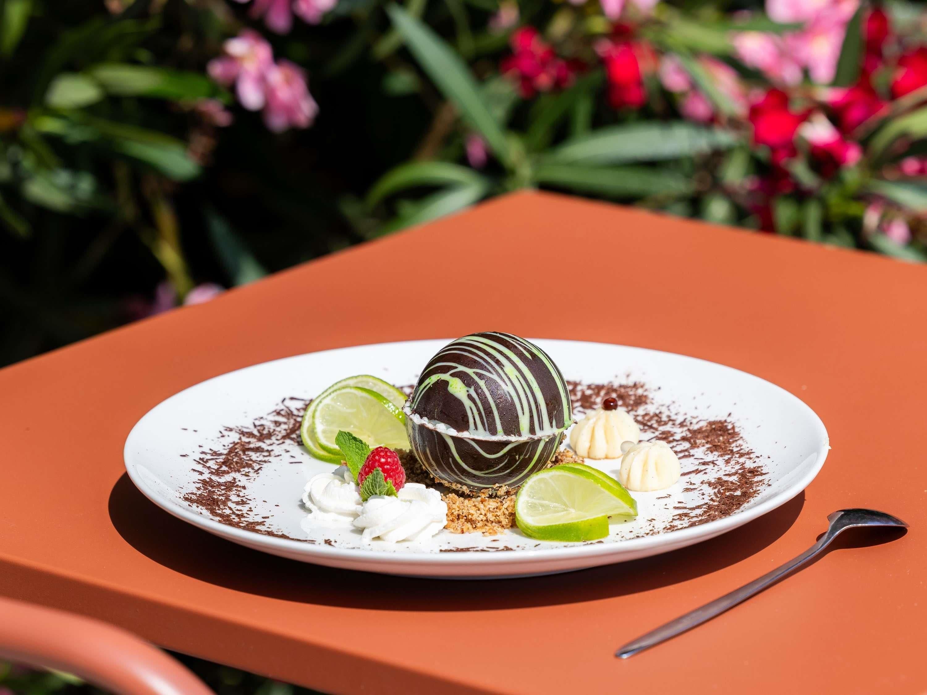 Dessert op een wit bord met limoen, slagroom en chocolade, op een oranje tafel.