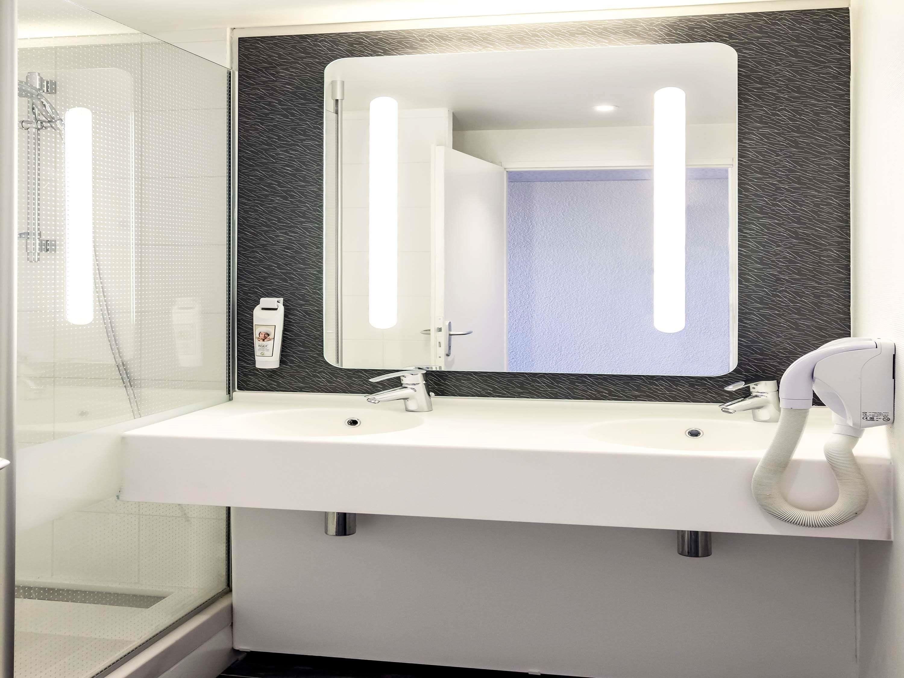 Ein modernes Badezimmer mit zwei Waschbecken, einem großen Spiegel und einem Fön.