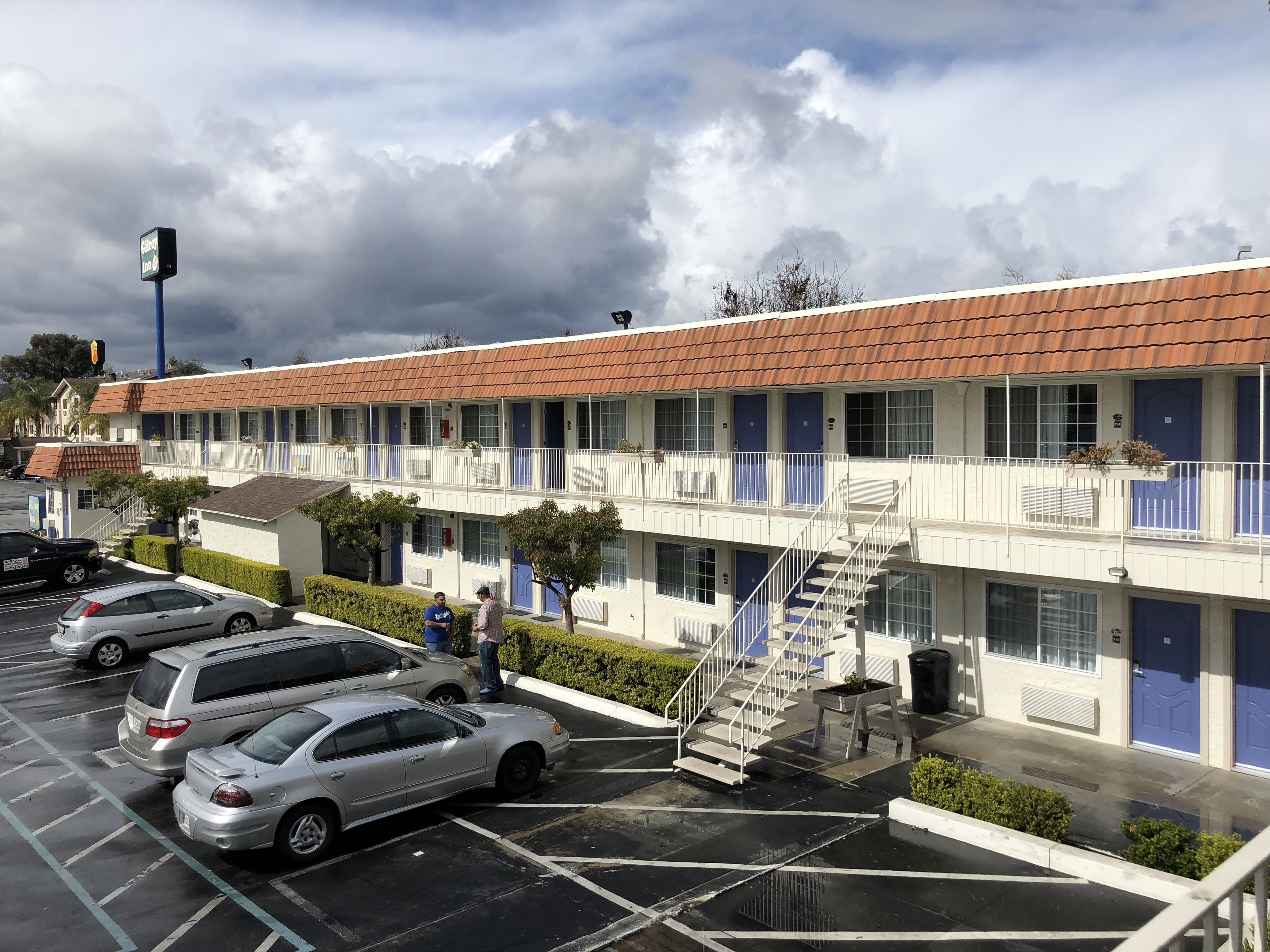 A motel with a row of rooms, a parking lot, and a staircase leading to the upper floor.