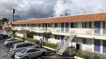 A motel with a row of rooms, a parking lot, and a staircase leading to the upper floor.
