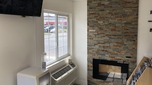 Una habitación de esquina con un ventanal grande, chimenea empotrada y televisor montado.