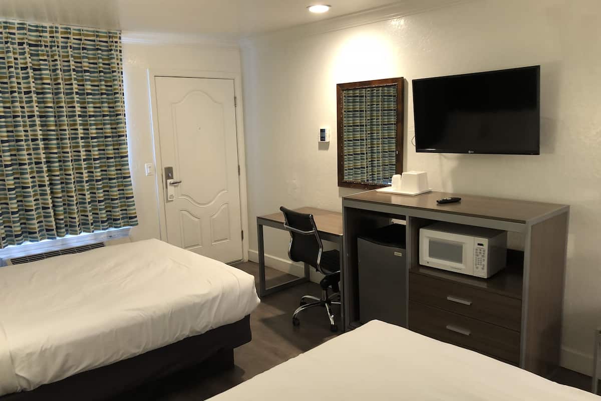 A hotel room with two beds, a desk with a chair, a television, and a microwave.