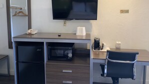 Una habitación de hotel con escritorio, televisión, refrigerador, microondas, cafetera y una silla.