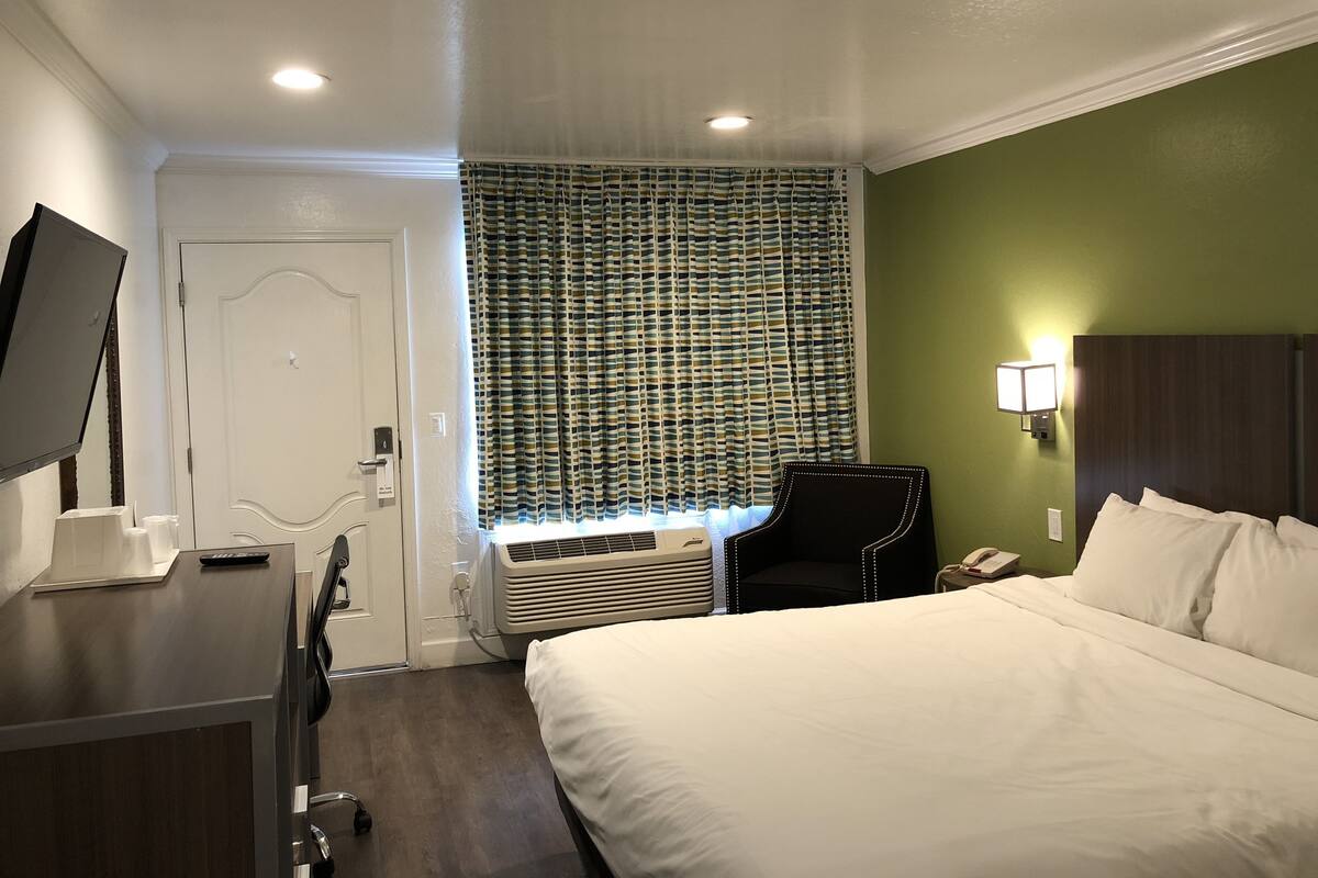 A hotel room with a bed, a desk, a chair, a TV, a window with curtains, and a wall-mounted phone.
