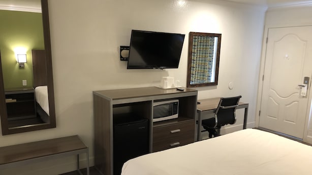Una habitación de hotel con cama, escritorio, computadora, televisor, microondas y puerta.