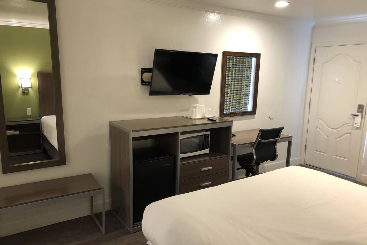 A hotel room with a bed, a desk with a computer, a TV, a microwave, and a door.