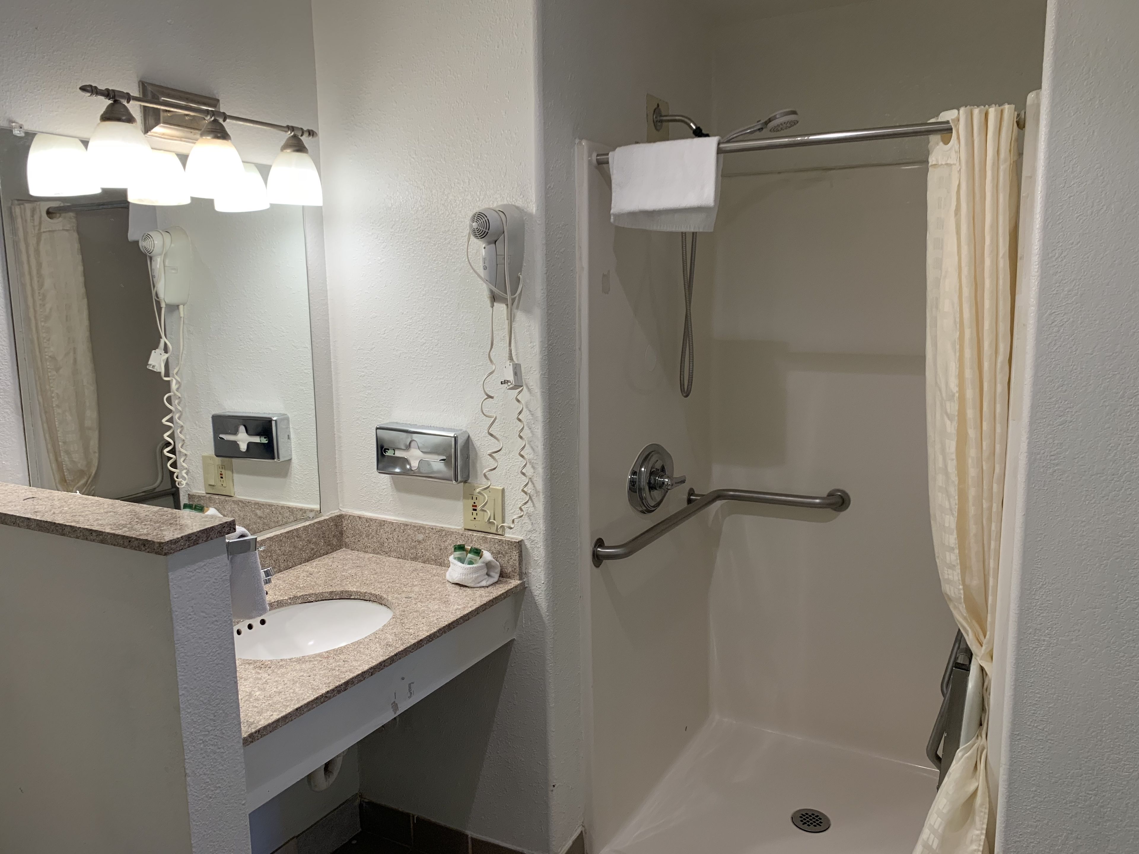 A bathroom with a sink, mirror, towel rack, shower, and hand dryer.
