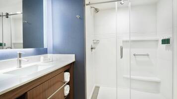 Un baño con un espejo grande, un lavamanos, cabina de ducha y un perchero para toallas.