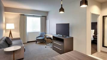 A modern hotel room with a sofa, desk, television, and a dining table.