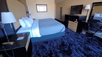 Una habitación de hotel con cama, escritorio, silla, televisor y espejo.