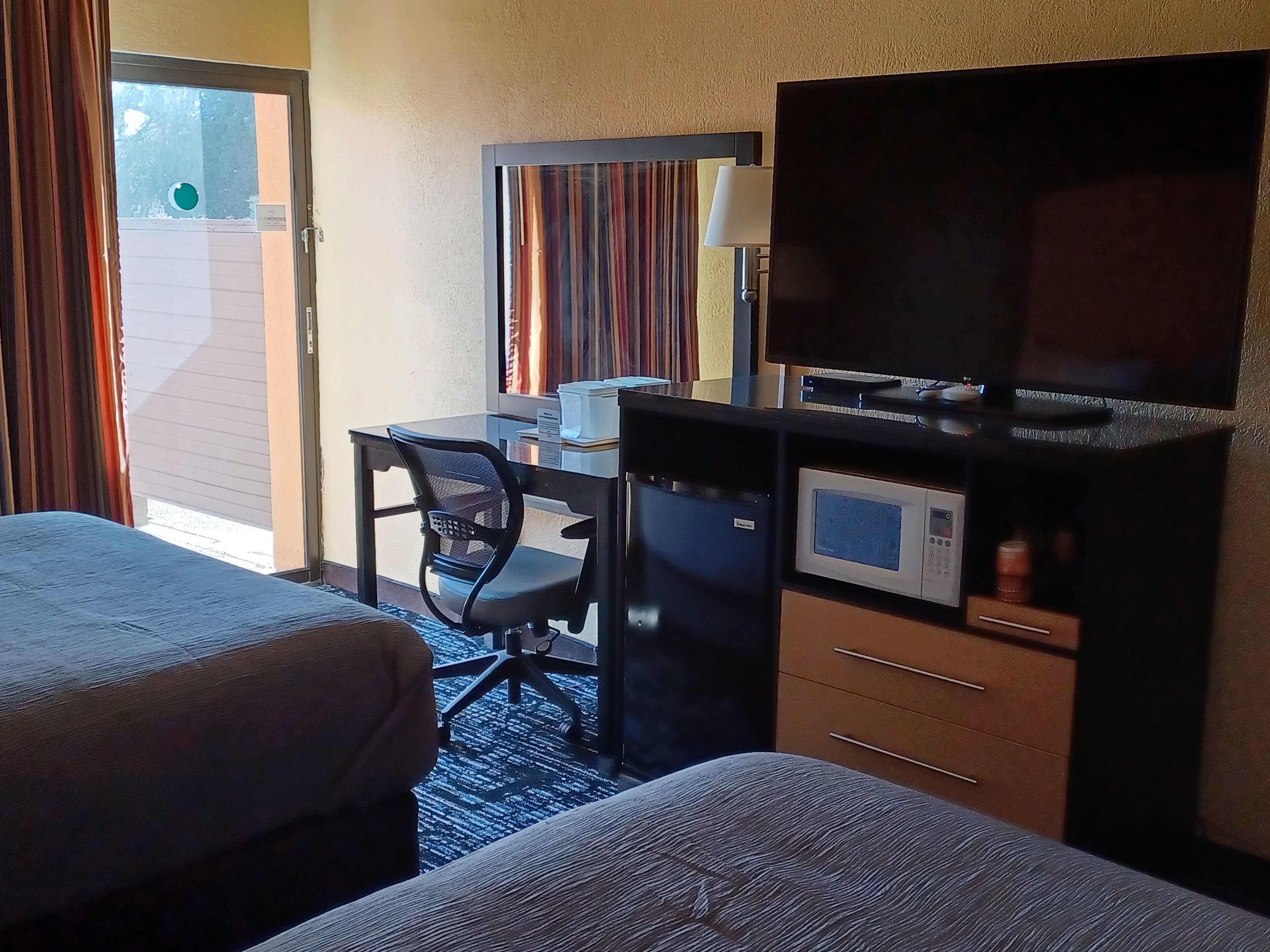 A hotel room with two beds, a desk with a computer, a microwave, and a TV.