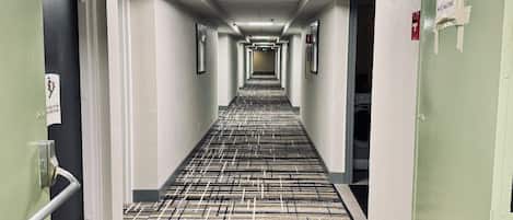 A long, narrow hallway with an exit sign overhead, a fire exit sign on the left, and a fire extinguisher on the right.