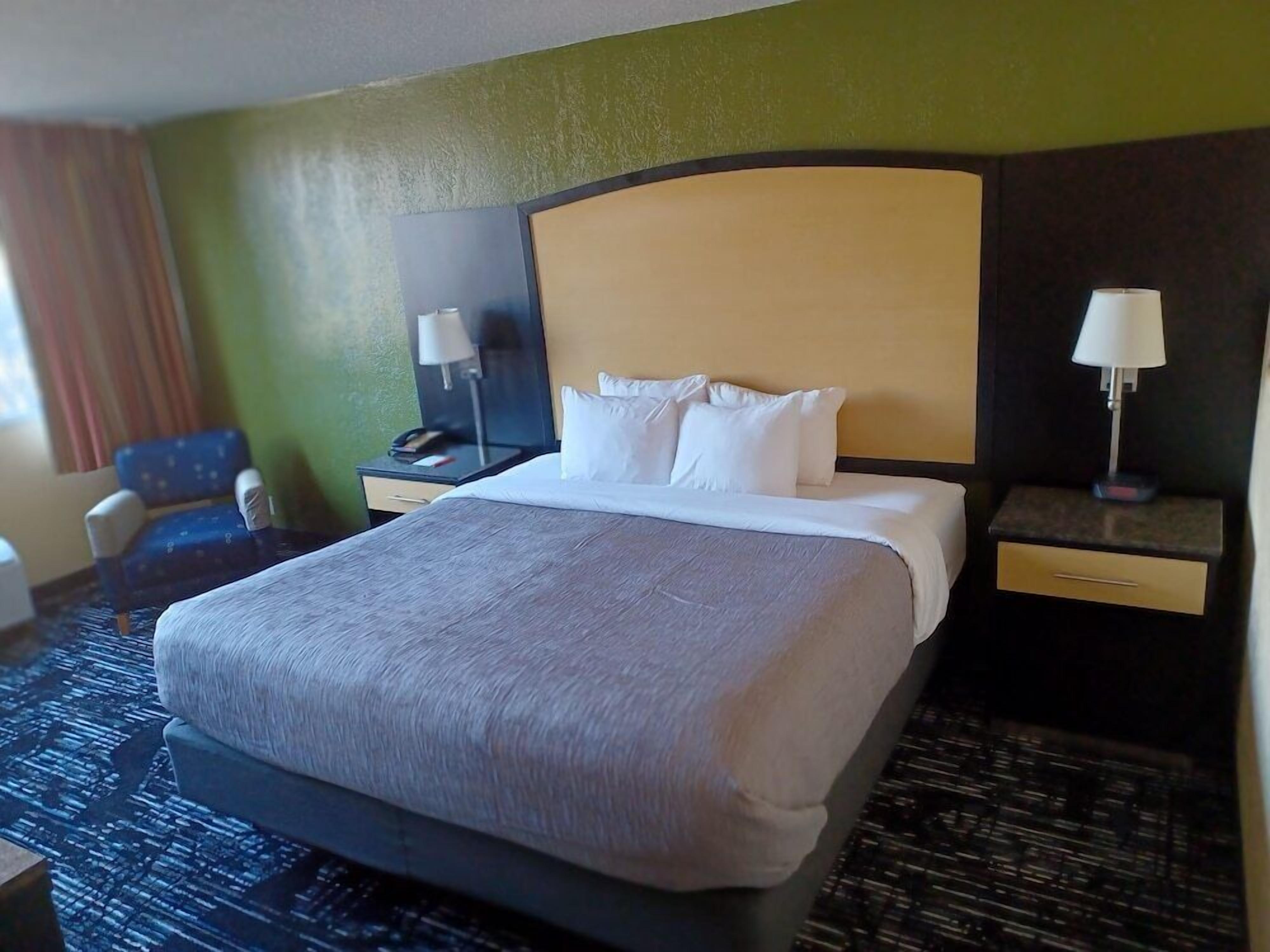 Habitación de hotel con una cama grande, una silla, un escritorio con lámpara y una mesita de noche con teléfono.