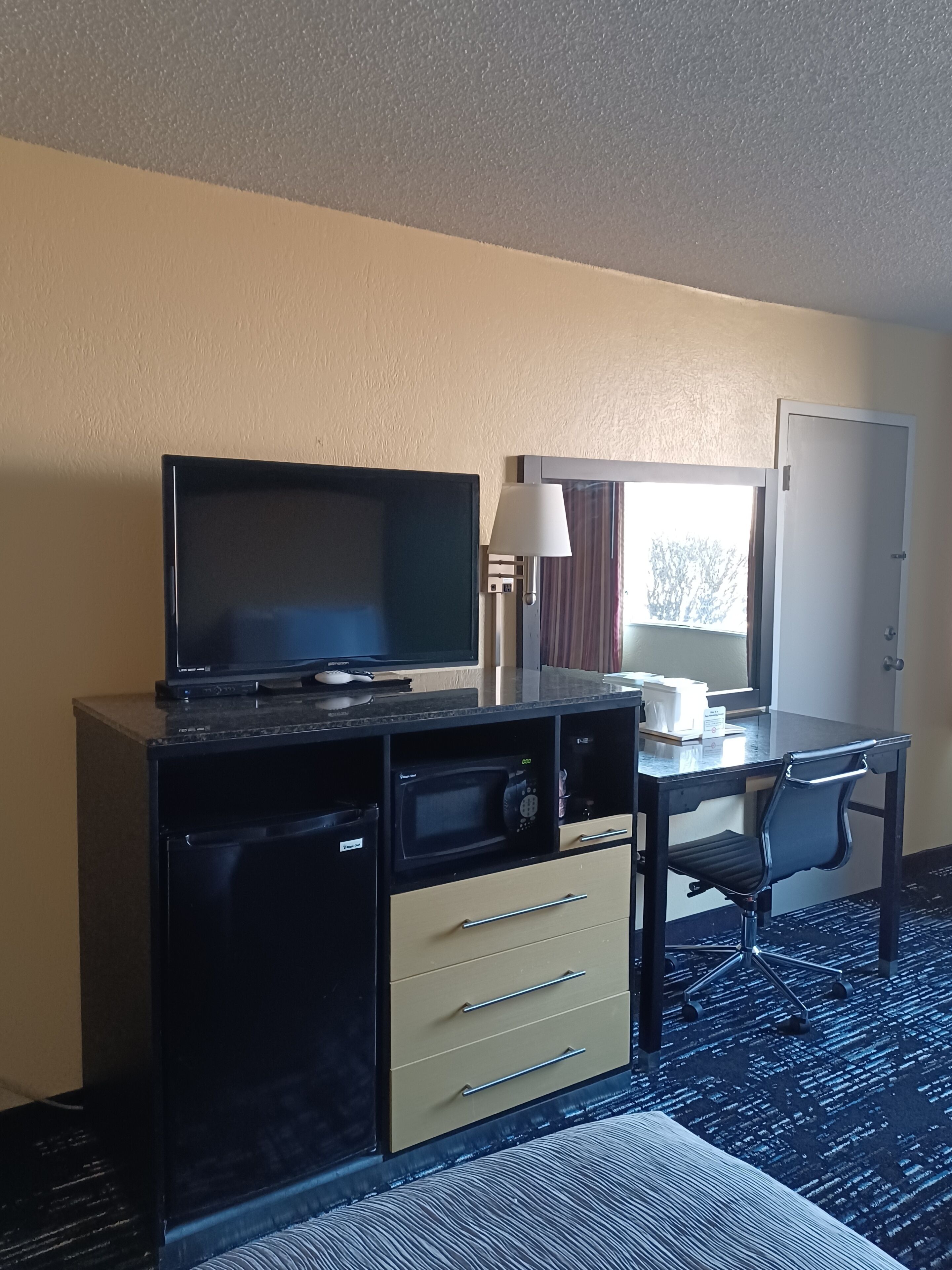 Habitación de hotel con televisor, escritorio, silla, microondas y puerta.
