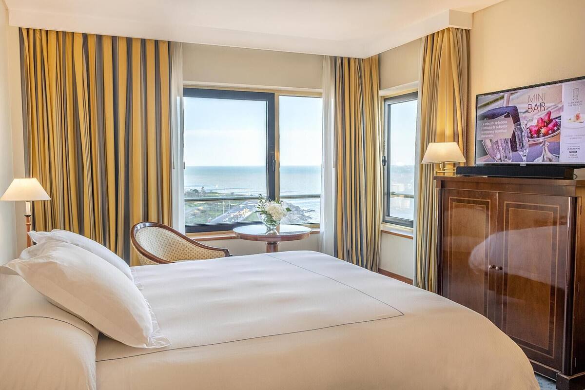 A hotel room with a large bed, a desk, a chair, and a view of the ocean.