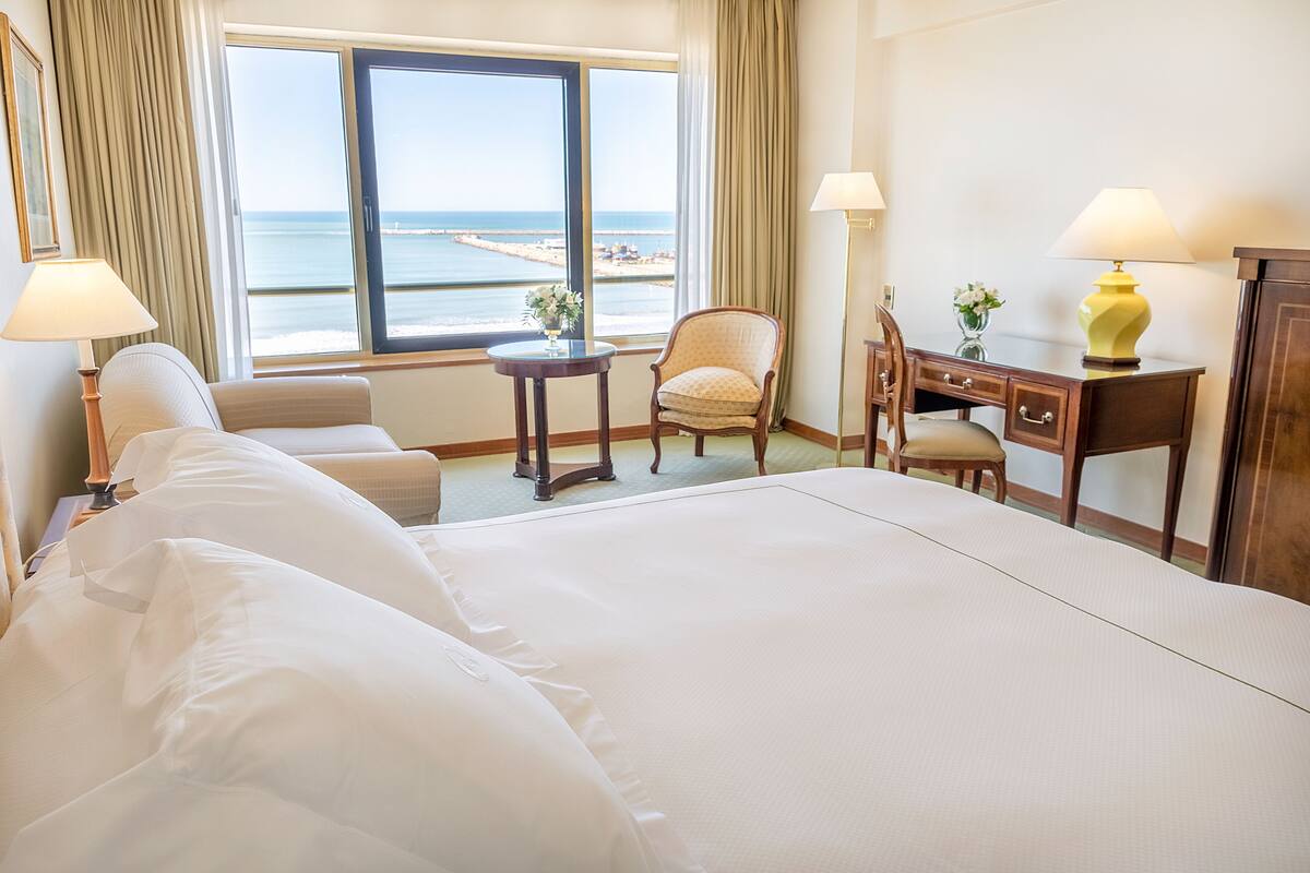 A hotel room with a large bed, a desk, a chair, and a view of the ocean.