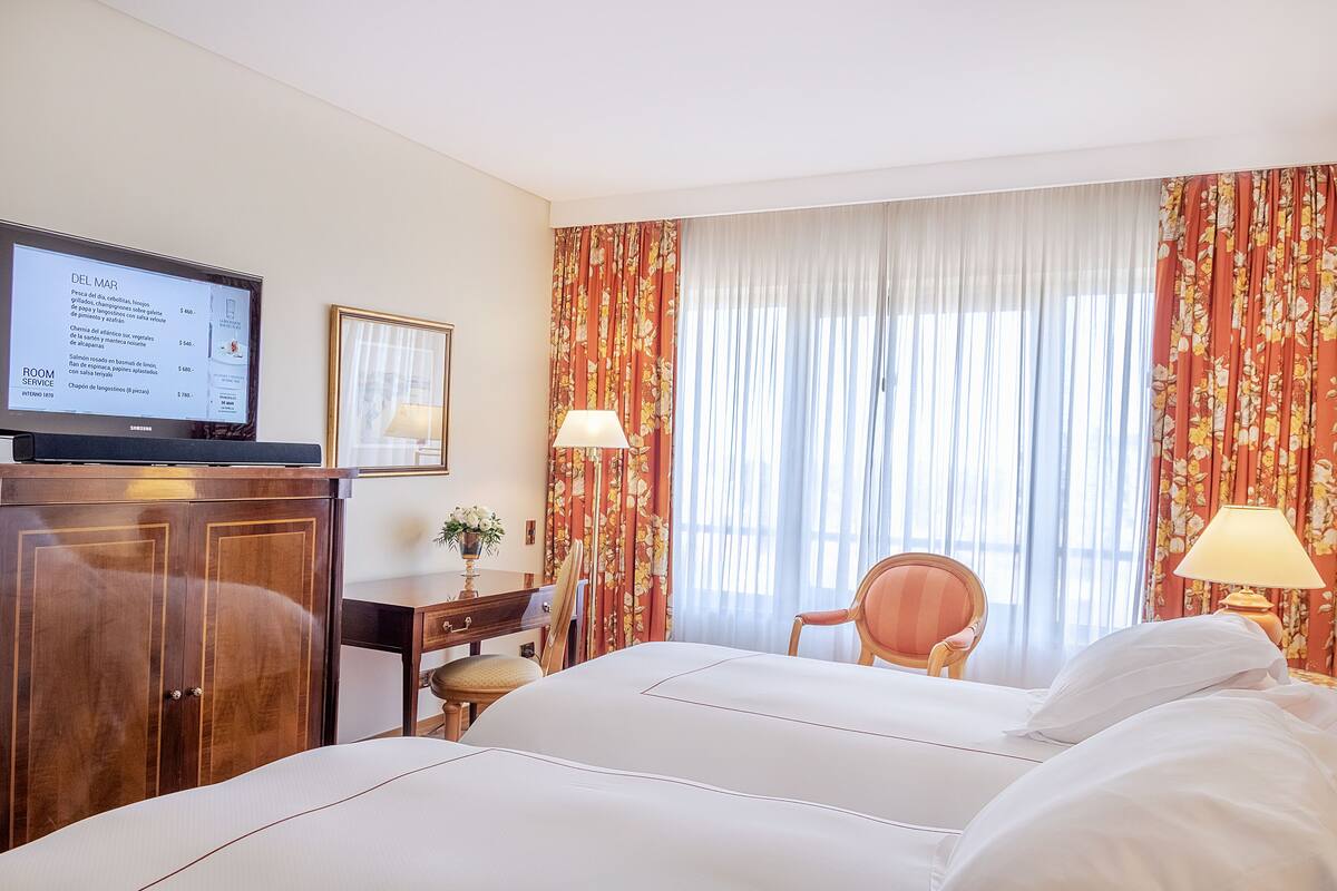 A hotel room with a bed, a desk with a computer, a television, and a window with curtains.