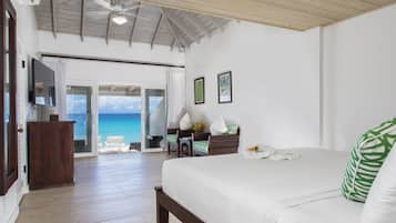 A spacious bedroom with a large bed, a wooden ceiling, a television, and a view of the ocean through a sliding door.