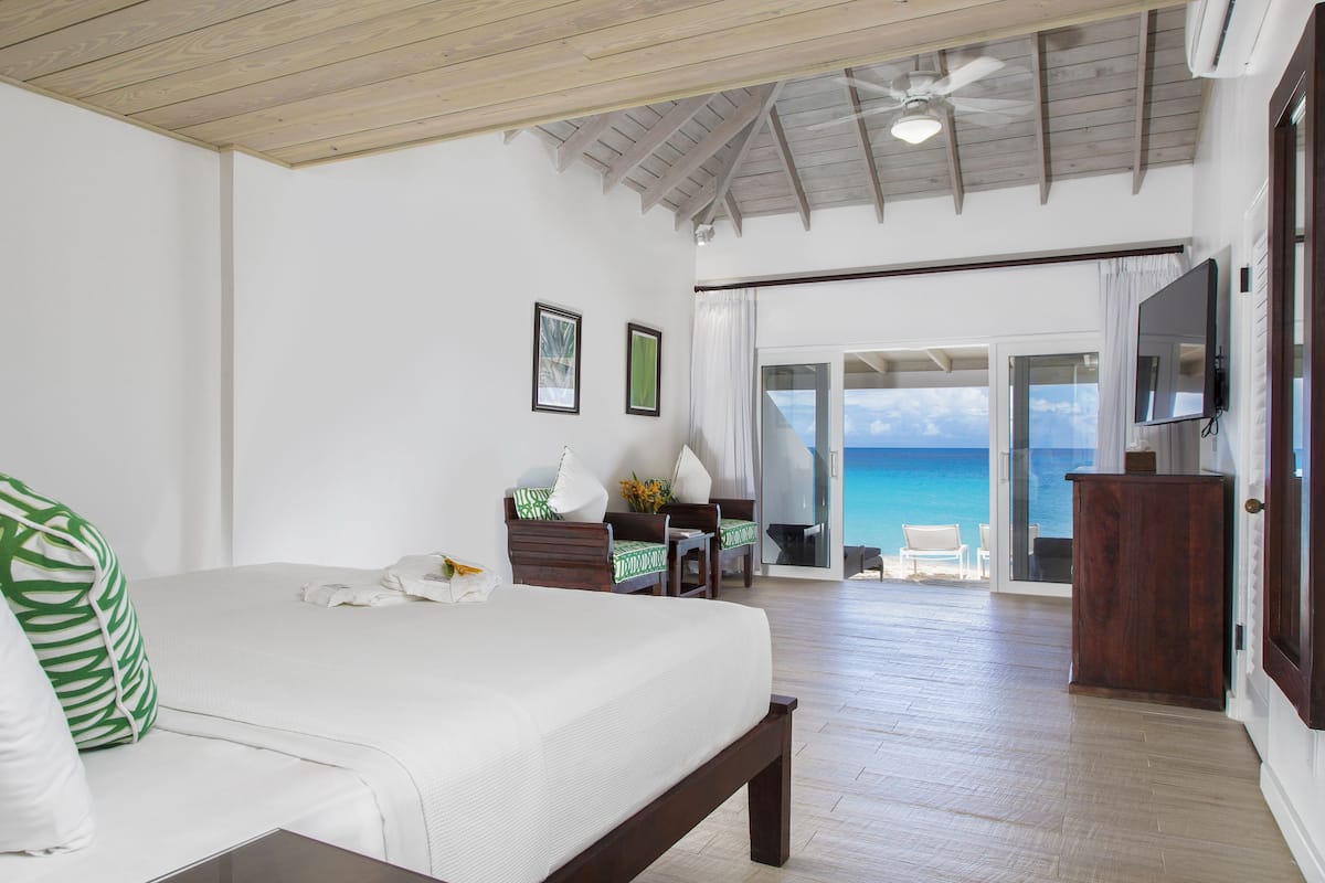 A bedroom with a bed, a wooden ceiling, a TV, and a view of the ocean.