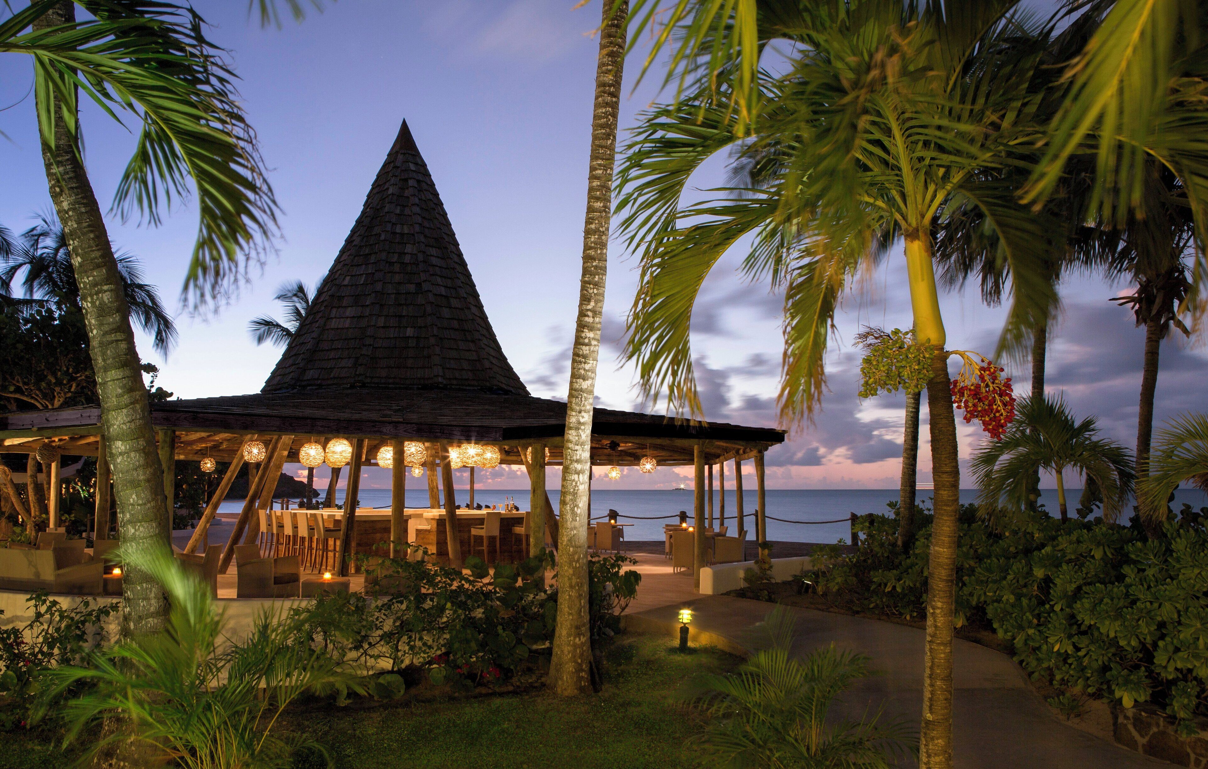 A beachside restaurant with a conical roof, outdoor seating, and views of the ocean.