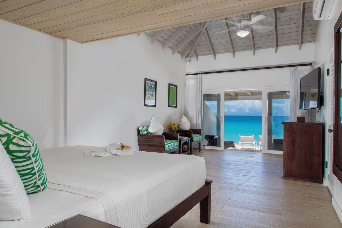 A bedroom with a large bed, a ceiling fan, and a view of the ocean through a sliding glass door.
