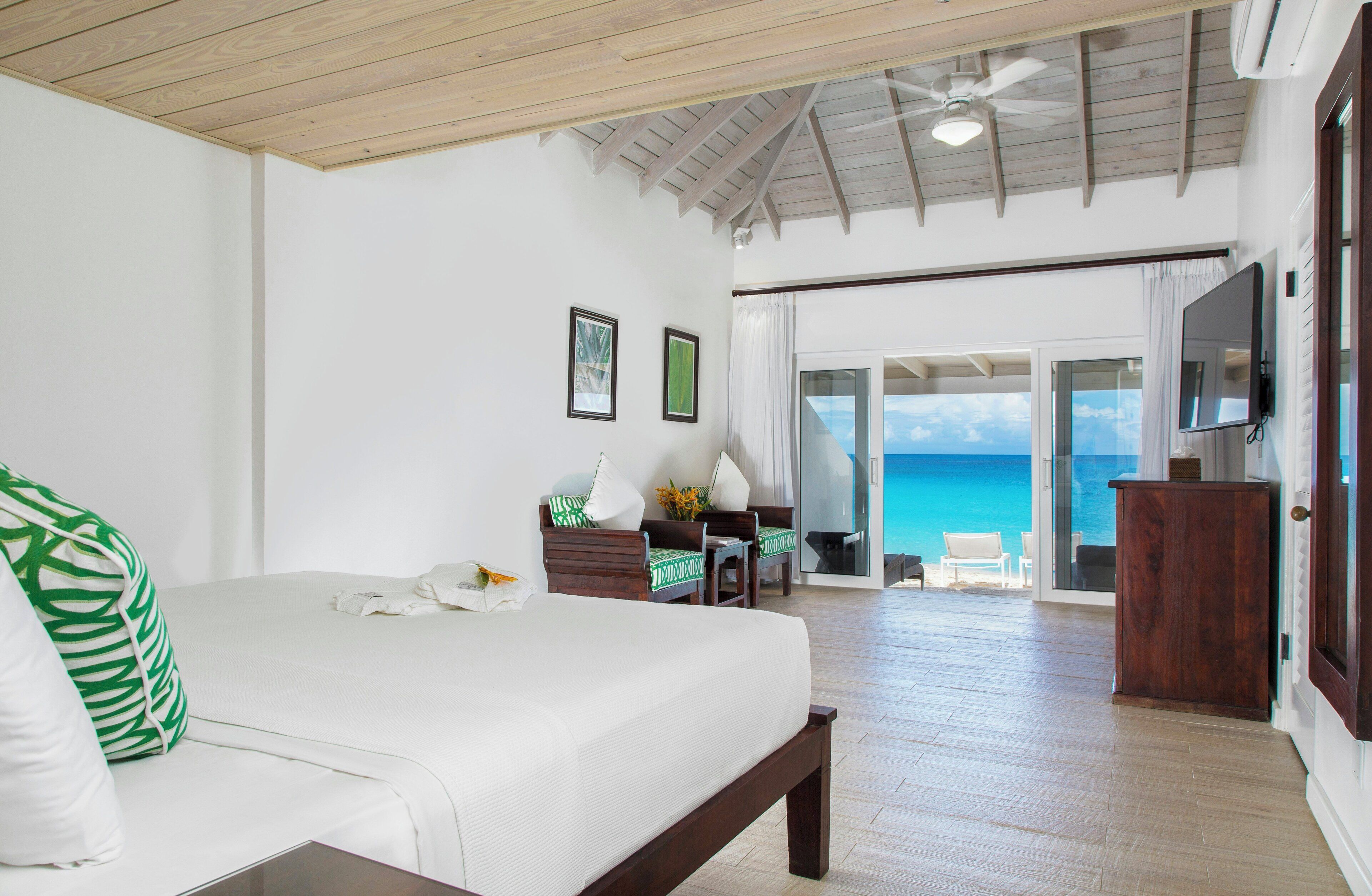 A bedroom with a large bed, a ceiling fan, and a view of the ocean through a glass door.