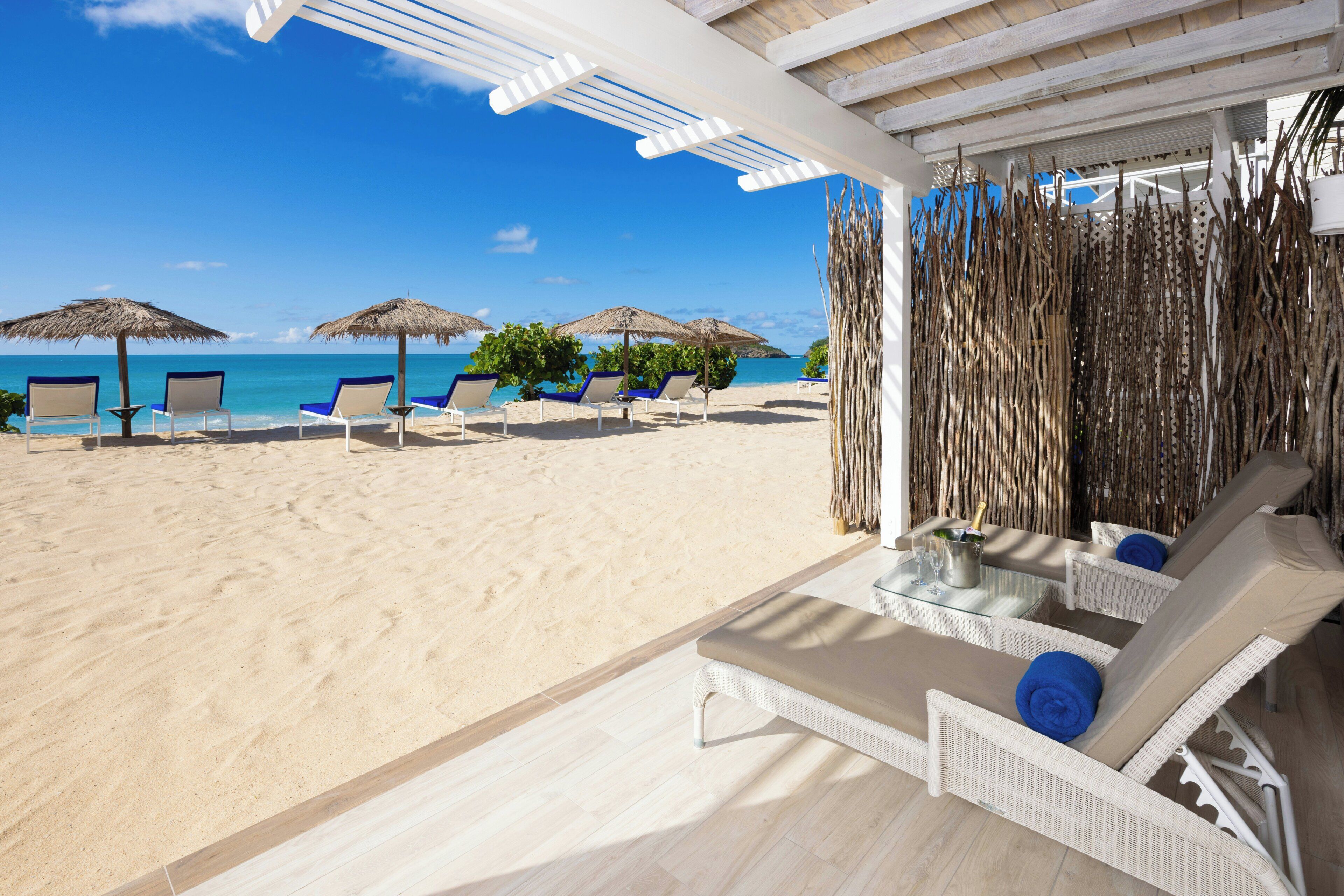 Eine Strandlounge mit Liegestühlen und Sonnenschirmen mit Blick auf einen Sandstrand und das Meer.