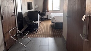Habitación de hotel con cama, escritorio con silla, televisor y ventana con cortinas.