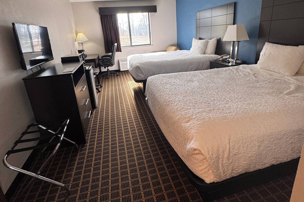Een hotelkamer met twee bedden, een bureau met stoel, een televisie en een raam met gordijnen.