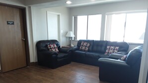 Una sala de estar con un sofá y un sillón de cuero negro, y una puerta de madera que indica 'SOLO PERSONAL'.
