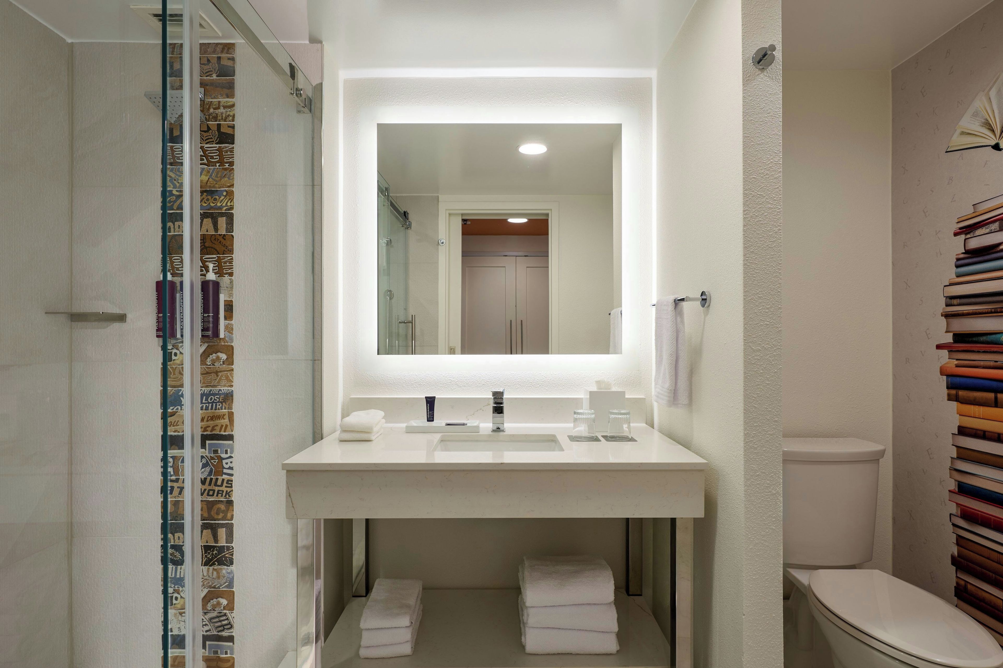 A bathroom with a white sink, mirror, and toilet. There is a glass shower enclosure and a towel rack with towels.