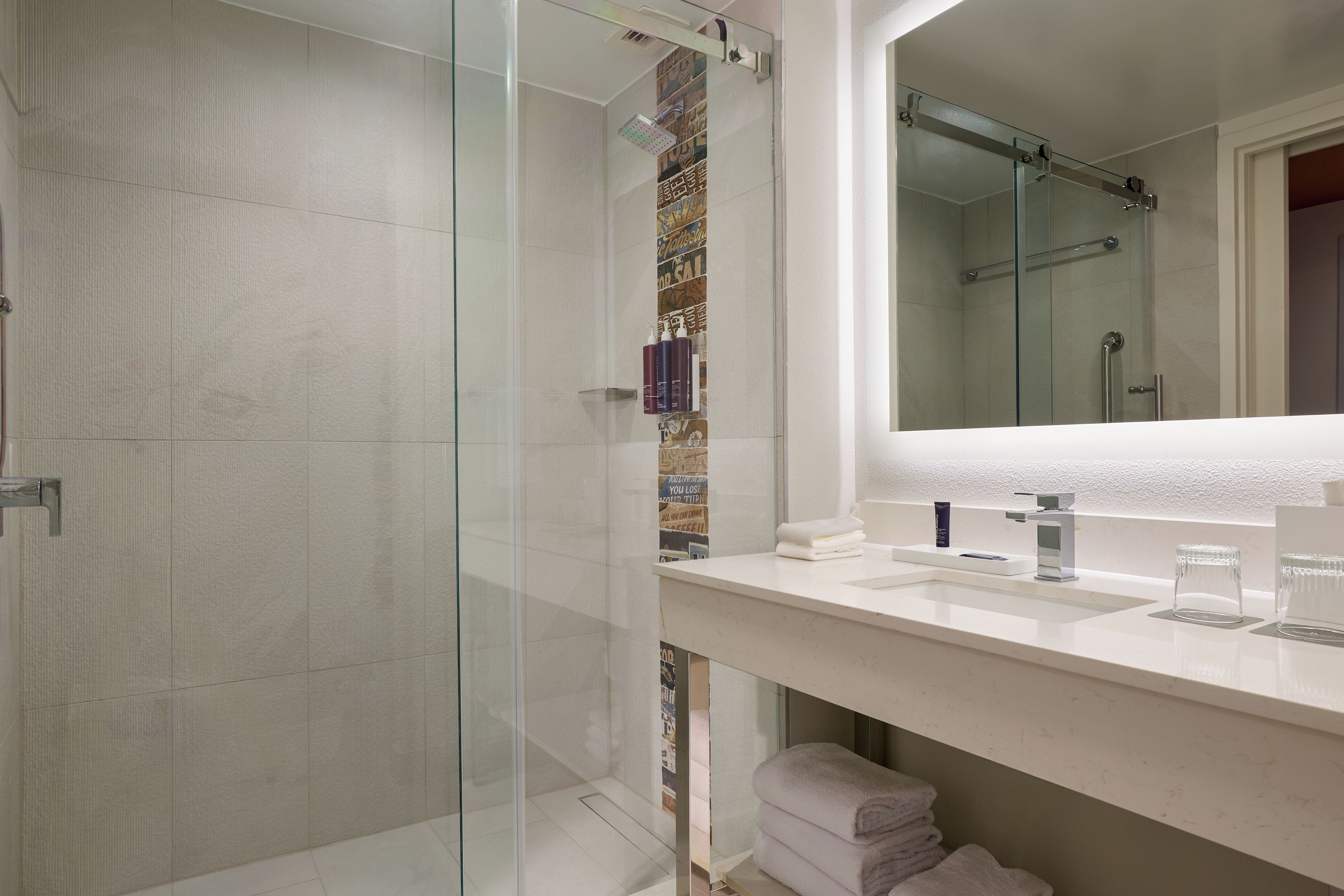 Een moderne badkamer met een douchecabine van glas, een witte wastafel met spiegel en een handdoekrek.