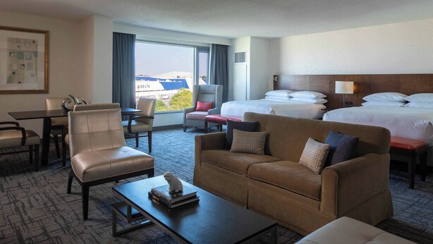 A hotel room with a sofa, armchair, dining table, and a bed with two pillows. - Renaissance Concourse Atlanta Airport Hotel (Atlanta)