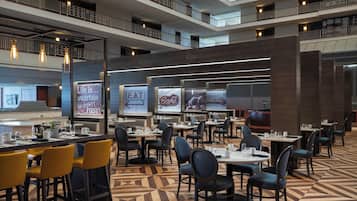 A modern dining area with multiple tables and chairs, a geometric patterned floor, and a view of the upper floors.
