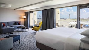 A hotel room with a large bed, a sofa, a chair, a small table, and a view of the airport. - Renaissance Concourse Atlanta Airport Hotel (Atlanta)