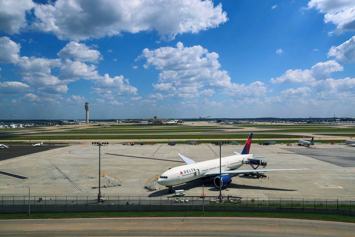 A Delta airplane parked on an airport tarmac with a clear sky and clouds in the background.