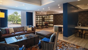 A modern living room with a leather sofa, a coffee table with chess set, a bookshelf, and a dining area. - Renaissance Concourse Atlanta Airport Hotel (Atlanta)