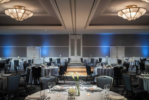 A banquet hall with round tables, chairs, and chandeliers.