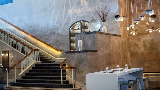 A modern hotel lobby with a staircase, a reception desk, and a wall with a 'Renaissance' sign. - Renaissance Concourse Atlanta Airport Hotel (Atlanta)