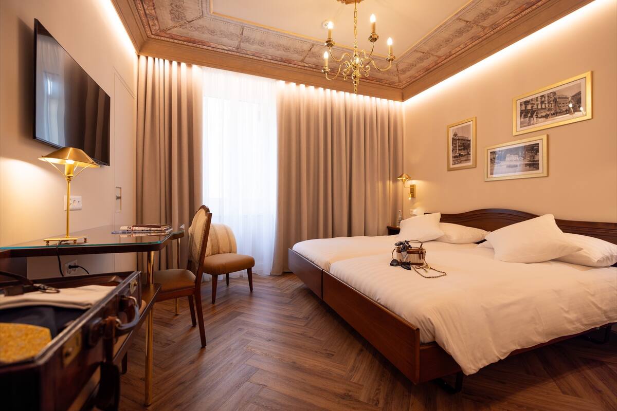 Une chambre d’hôtel avec un lit, un bureau, une chaise, une télévision et un lustre.