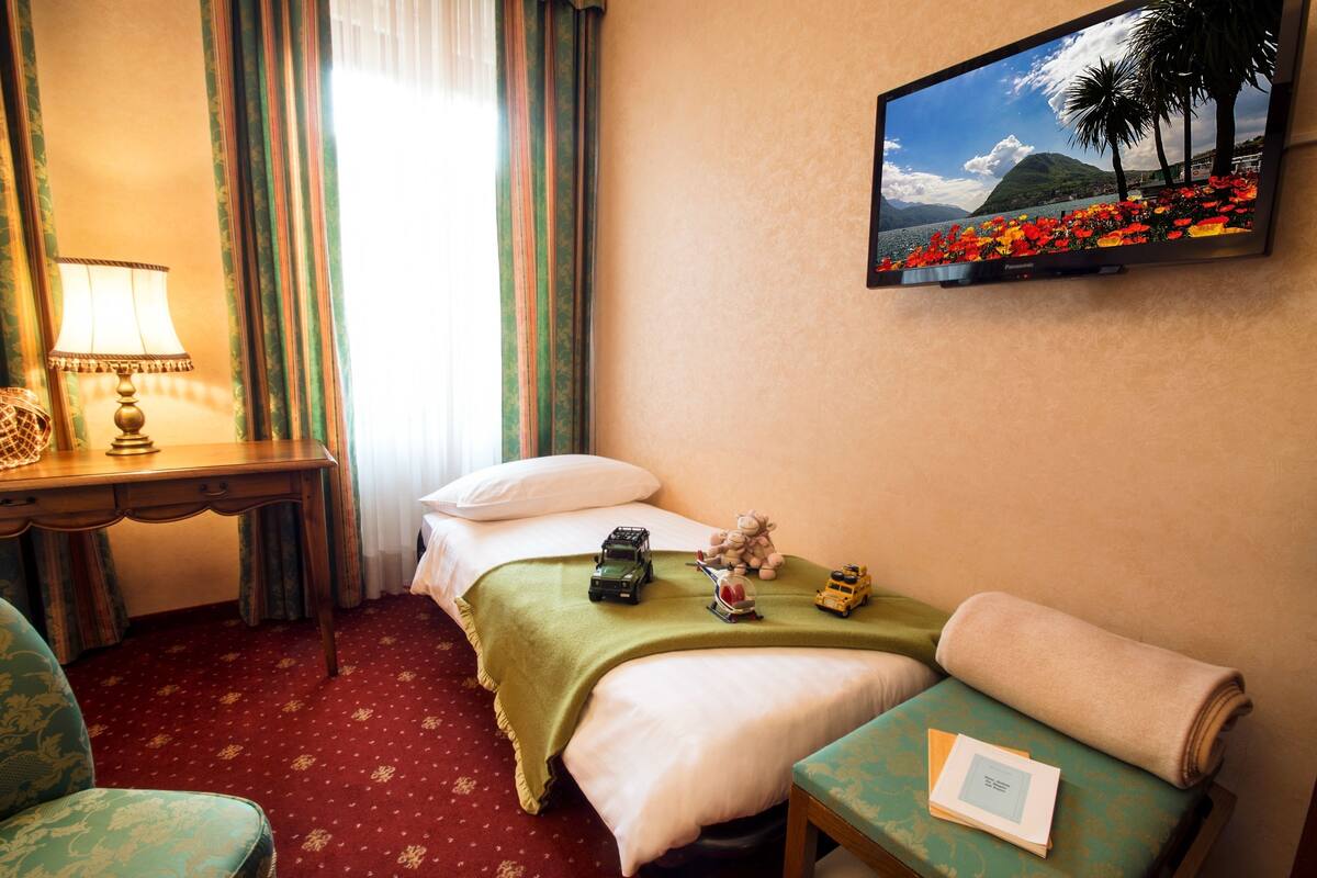 Une chambre d’hôtel avec un lit, un bureau doté d’une lampe, un téléviseur diffusant une scène de plage et une chaise avec un livre.