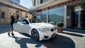 En vit BMW stod parkerad framför ett hotell med en skylt där det stod ”HOTEL INTERNATIONAL”.