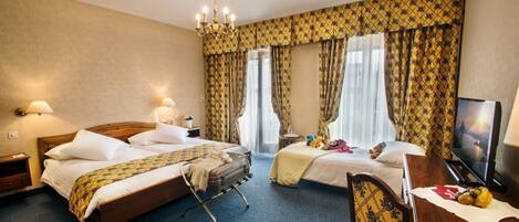 A hotel room with two beds, a desk, a TV, and a chandelier.