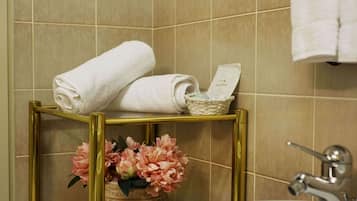 Ein Badezimmer mit beigen Fliesen, einem goldfarbenen Waschtisch und einem weißen Waschbecken, sowie einer dekorativen Vase mit rosa Blumen.