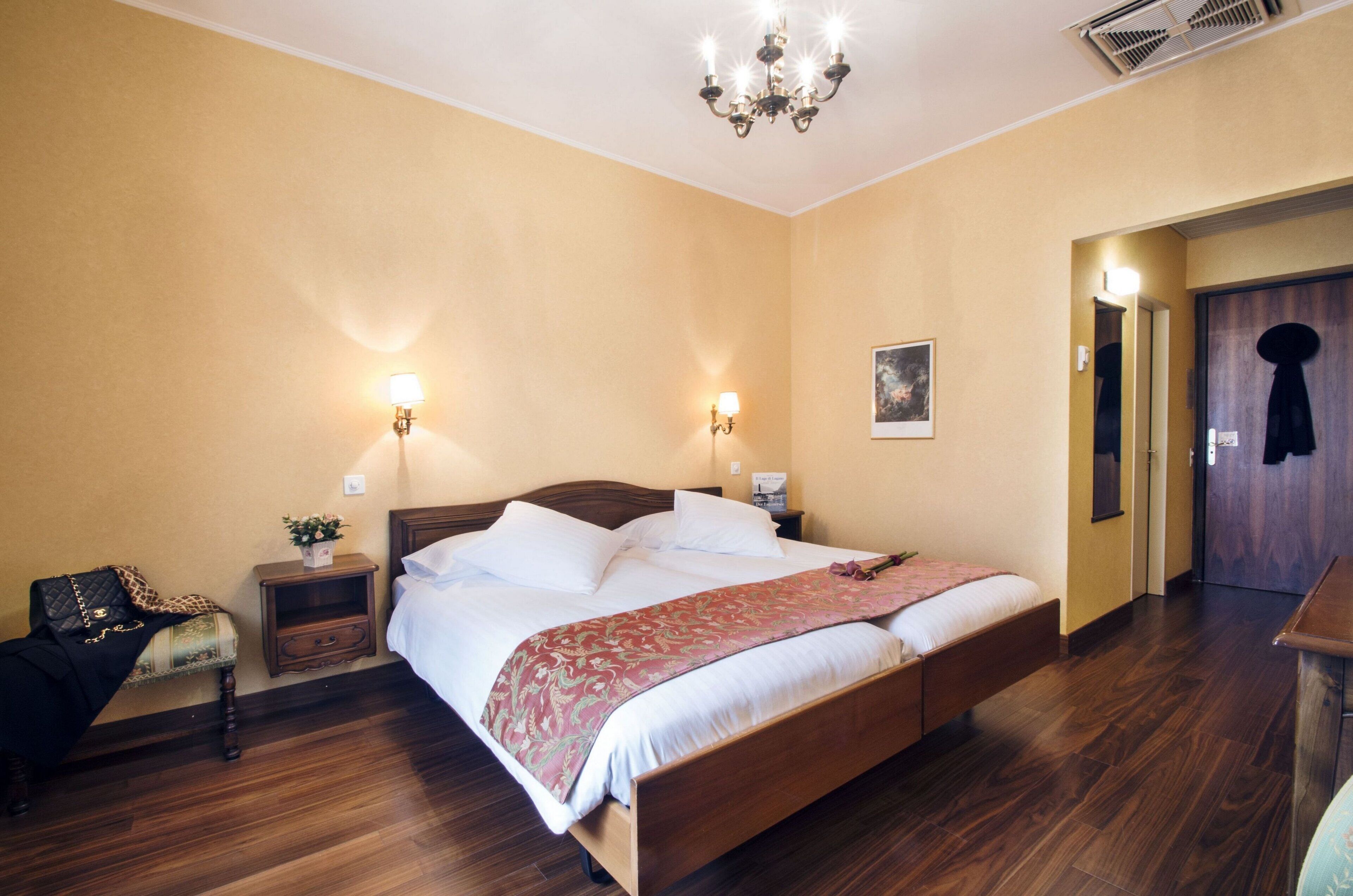 A hotel room with a wooden bed, bedside lamps, a nightstand, a chair, and a door.